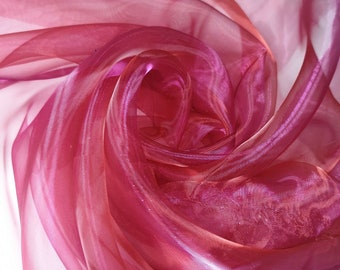 May include: A close-up of a pink and orange sheer fabric with a shimmery finish. The fabric is draped and folded, creating a soft and delicate texture.