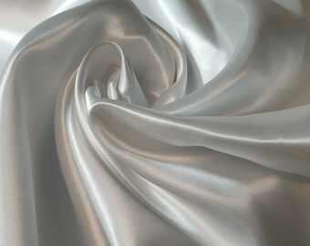 May include: White satin fabric with a smooth, silky texture. The fabric is draped and folded, creating soft, flowing curves.
