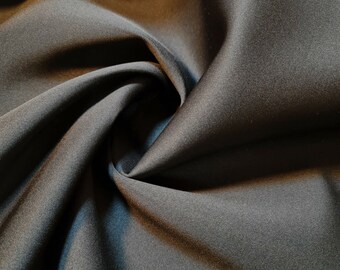 May include: Close-up of a smooth, black fabric with a soft, silky texture. The fabric is draped and folded, creating a luxurious and elegant look.