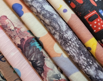 May include: A collection of fabric swatches in various colors and patterns, including floral, geometric, and abstract designs. The swatches are arranged in a stack, with the top swatch being a black fabric with white polka dots.