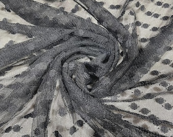 May include: A sheer black fabric featuring a repeating pattern of small, raised black dots. The material is arranged in a swirling, gathered formation, highlighting the fine, translucent mesh texture and the consistent distribution of the dark spots.