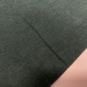 May include: A close-up of a dark green fabric with a straight seam running diagonally across the surface.