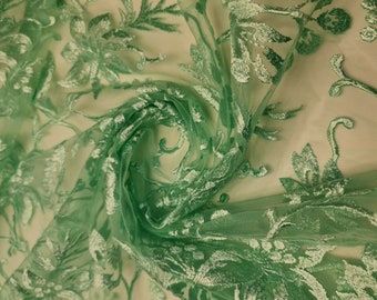 May include: Green floral lace fabric with a delicate pattern. The fabric is sheer and has a soft, flowing texture.