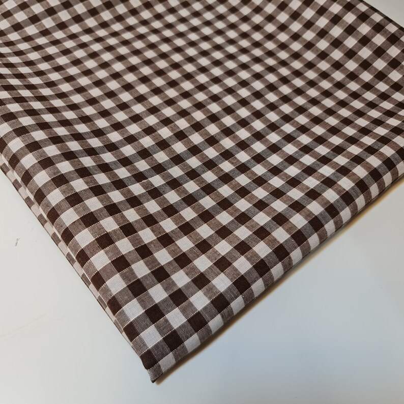 May include: Brown and white gingham fabric with a checkered pattern. The fabric is folded and has a soft, textured surface.
