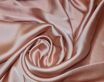 May include: A close-up of a soft, smooth, rose-colored fabric with a silky texture. The fabric is draped and folded, creating a luxurious and elegant look.