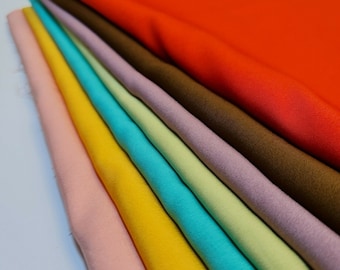 May include: A stack of fabric swatches in various colors, including red, brown, purple, green, blue, yellow, and pink. The fabric is smooth and appears to be a woven material.