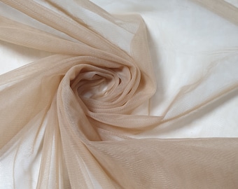 May include: A close-up of a sheer, beige fabric with a soft, delicate texture. The fabric is draped and folded, creating a flowing, elegant look.