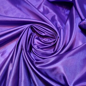 Könnte beinhalten: Nahaufnahme eines violetten Satin-Stoffes mit einer glatten, seidenartigen Textur. Der Stoff ist drapiert und gefaltet und erzeugt ein wirbelndes Muster.