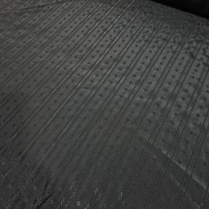 Puede incluir: Una tela negra que presenta un patrón repetitivo de rayas verticales y pequeñas formas de diamante. El material tiene un brillo sutil y una superficie texturizada con detalles finos e intrincados en todo el tejido, creando una estética oscura.