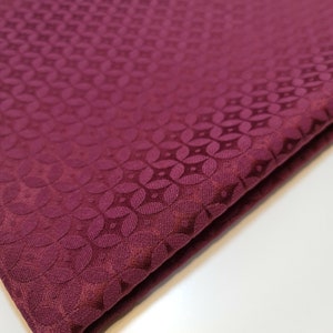 May include: Burgundy fabric with a repeating embossed pattern of small circles and leaves.
