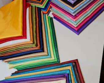 Może przedstawiać: Stos kolorowych próbek tkanin w różnych odcieniach niebieskiego, zielonego, czerwonego, żółtego i brązowego. Tkanina jest ułożona wachlarzowo, z najciemniejszymi kolorami na dole i najjaśniejszymi na górze.