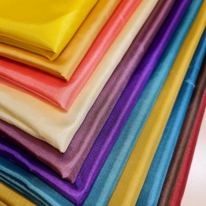 May include: A stack of colourful satin fabric swatches in various shades of yellow, orange, pink, purple, blue, and brown.