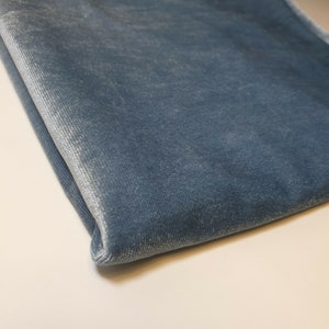 May include: A close-up of a folded piece of blue velvet fabric. The fabric has a subtle sheen and a soft, plush texture.