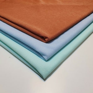 May include: Three fabric swatches stacked on top of each other. The top swatch is a brown color, the middle swatch is a light blue color, and the bottom swatch is a light green color.
