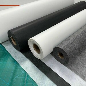 Könnte beinhalten: Vier Rollen Stoff in verschiedenen Farben und Texturen. Die Rollen sind weiß, schwarz, grau und weiß. Der Stoff ist wahrscheinlich Einlage, eine Art schmelzbarer Stoff, der beim Nähen und Quilten verwendet wird.