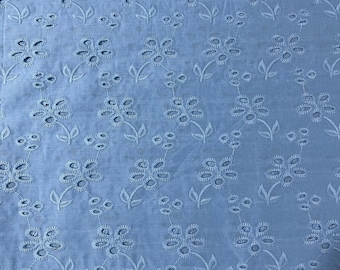 May include: A light blue fabric featuring an all-over eyelet embroidery pattern. The design consists of repeating floral motifs with five-petaled flowers and small leaves, created with cut-out holes and tonal stitching throughout the material.