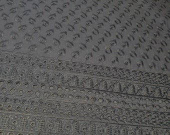 May include: Black fabric with a repeating pattern of small, embroidered flowers. The fabric has a scalloped edge with a repeating pattern of small circles and ovals.