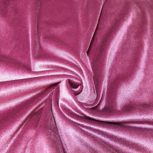 May include: Close-up of a soft, pink velvet fabric with a subtle ribbed texture. The fabric is draped and folded, creating a luxurious and elegant look.
