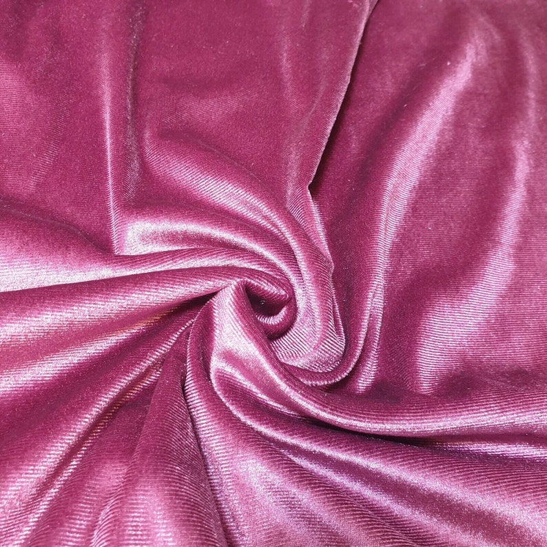 May include: Close-up of a soft, pink velvet fabric with a subtle ribbed texture. The fabric is draped and folded, creating a luxurious and elegant look.