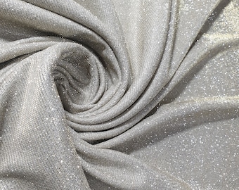 May include: Close-up of a silver sparkly fabric with a textured, ribbed surface. The fabric is folded and draped, creating a soft, flowing look.