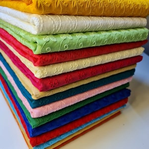 May include: A stack of 20 different coloured fabric swatches with an embroidered floral pattern. The fabrics are arranged in a rainbow order from yellow to blue.