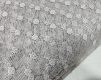 May include: A light gray sheer mesh fabric featuring a repeating pattern of small, opaque white circular dots. The material has a fine, net-like texture with a consistent grid structure throughout, creating a semi-transparent appearance across the surface.