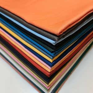 May include: A stack of fabric swatches in various colors, including orange, yellow, pink, red, blue, green, and brown. The fabric is folded neatly and arranged in a diagonal pattern.