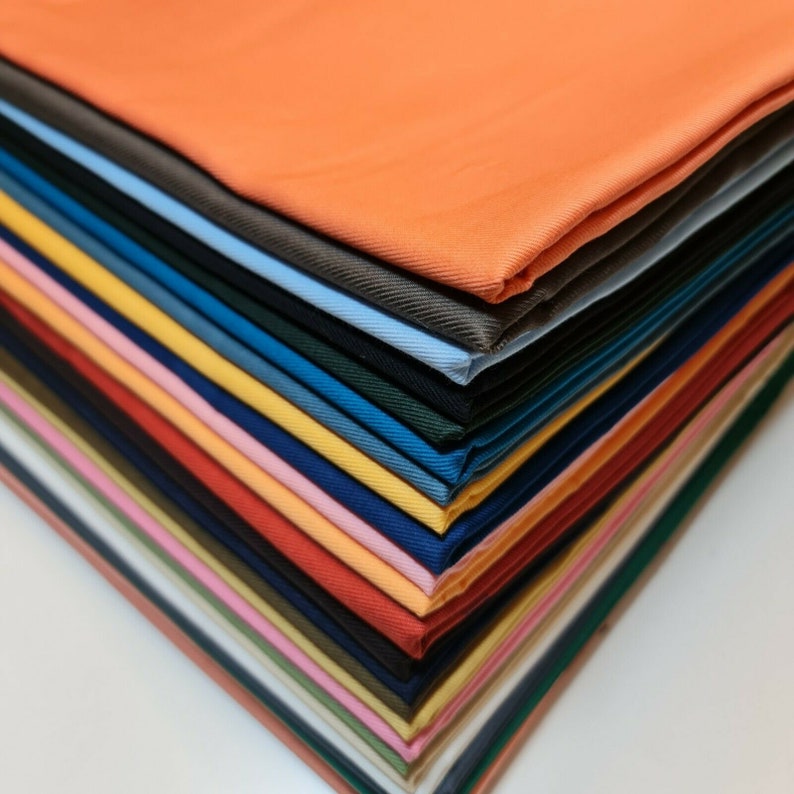 May include: A stack of fabric swatches in various colors, including orange, yellow, pink, red, blue, green, and brown. The fabric is folded neatly and arranged in a diagonal pattern.