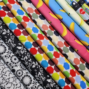 May include: A collection of colorful fabric swatches with geometric patterns, floral designs, and a pattern of yellow bananas. The fabrics are arranged in a fan shape, with the most colorful fabrics at the top and the more subtle fabrics at the bottom.
