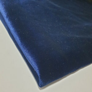 May include: A close-up of a folded piece of dark blue corduroy fabric. The fabric has a soft, velvety texture and a subtle ribbed pattern.