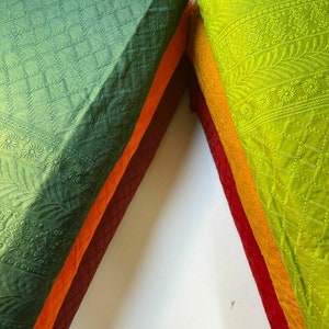 May include: Stack of fabric squares in various shades of green, orange, and red. The fabric has an embroidered pattern.