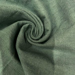May include: Close-up of a soft, green fabric with a textured weave. The fabric is folded and draped, creating a swirling pattern.