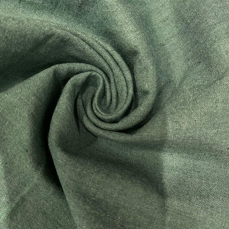 May include: Close-up of a soft, green fabric with a textured weave. The fabric is folded and draped, creating a swirling pattern.