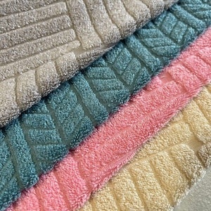 May include: Close-up of four textured bath towels in shades of gray, teal, pink, and yellow. Each towel features a repeating geometric pattern. The towels are soft and fluffy, ideal for bathroom decor.