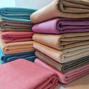 May include: A stack of folded fabric in various colors, including light blue, beige, pink, purple, and gray. The fabric is arranged in a neat pile, with the top layer folded over to reveal the color underneath.