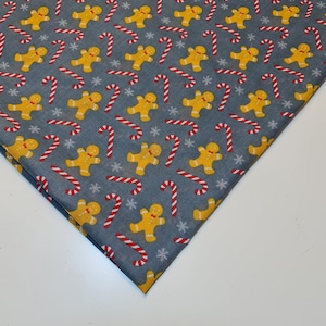May include: A grey fabric with a repeating pattern of gingerbread men and candy canes. The gingerbread men are yellow and the candy canes are red and white.