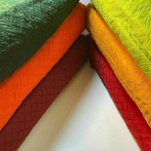 May include: A stack of six fabric swatches in various colours, including green, orange, maroon, and yellow. The fabric has a textured, quilted pattern.