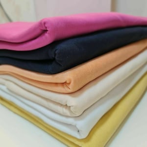 May include: A stack of six folded fabric swatches in various colors, including pink, navy blue, peach, cream, white, and yellow.