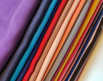 May include: A stack of fabric swatches in various colors, including purple, blue, red, pink, and yellow. The fabric is folded neatly and arranged in a gradient pattern.
