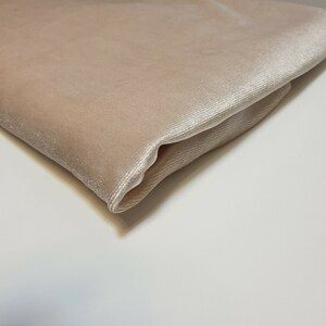 May include: A close-up of a folded piece of beige velvet fabric. The fabric has a subtle sheen and a soft, luxurious feel.