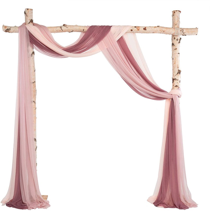 May include: A rustic wedding arch made of birch branches, draped with flowing fabric in shades of mauve, blush, and cream. The fabric is arranged in elegant folds, creating a romantic and airy feel for a ceremony backdrop.