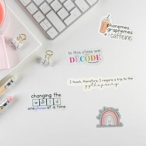 May include: Five vinyl stickers featuring educational themes. One shows a coffee cup with text phonemes graphemes caffeine. Another says In this class we DECODE. A third reads I teach, therefore, I require a trip to the zythepsary. One says changing the world one phoneme at a time. The last shows a rainbow with text be like schwa never stressed.