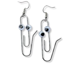 May include: A pair of quirky earrings featuring silver-toned paperclip designs. Each earring has a googly eye attached, giving them a playful, animated look. The earrings have a simple hook closure.