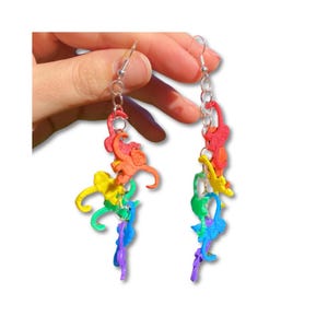 May include: Rainbow colored monkey dangle earrings. Each earring features five monkeys in a rainbow color scheme, hanging from a silver chain.