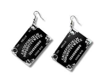 May include: A pair of rectangular drop earrings featuring a black and white spirit board design. Each earring displays the alphabet, numbers zero through nine, the words YES, NO, HELLO, and GOOD BYE, with decorative corner motifs and silver hooks.