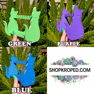 May include: Three cat-shaped, 3D printed, wall-mounted organizers in green, purple, and blue. Each organizer has two shelves and a cat silhouette design. The text "SHOPKROPED.COM" is visible in the background.