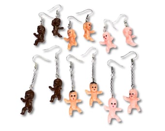 Op de afbeelding: Een set van 10 hangende oorbellen met kleine plastic babypoppen in verschillende huidtinten. De oorbellen zijn zilverkleurig en hebben een haaksluiting.