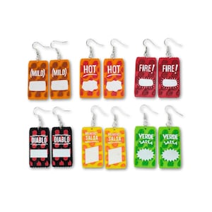 May include: A set of eight novelty earrings shaped like miniature salsa packets. The earrings feature various labels such as "Mild", "Hot", "Fire", "Diablo", "Breakfast Salsa", and "Verde Salsa". Each earring has a silver hook.