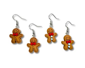 May include: Four gingerbread man earrings featuring brown figures with smiling faces, red bow ties, and small white buttons. Each charm hangs from a silver-toned metal fishhook ear wire, creating a set of dangling jewellery pieces.