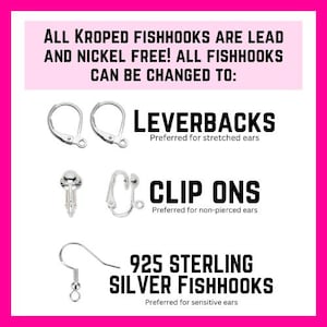 Puede incluir: Imagen de componentes de pendientes con texto. El texto dice: "&iexcl;TODOS LOS ANZUELOS KROPED SON LIBRES DE PLOMO Y N&Iacute;QUEL! TODOS LOS ANZUELOS SE PUEDEN CAMBIAR A: LEVERBACKS, CLIP ONS, 925 STERLING SILVER FISHHOOKS". La imagen est&aacute; sobre un fondo rosa.
